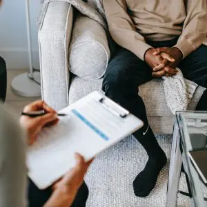 Bipolar disorder can be treated effectively with therapy and medication. A man sits on a sofa while a therapist holds a clipboard to perform an assessment.