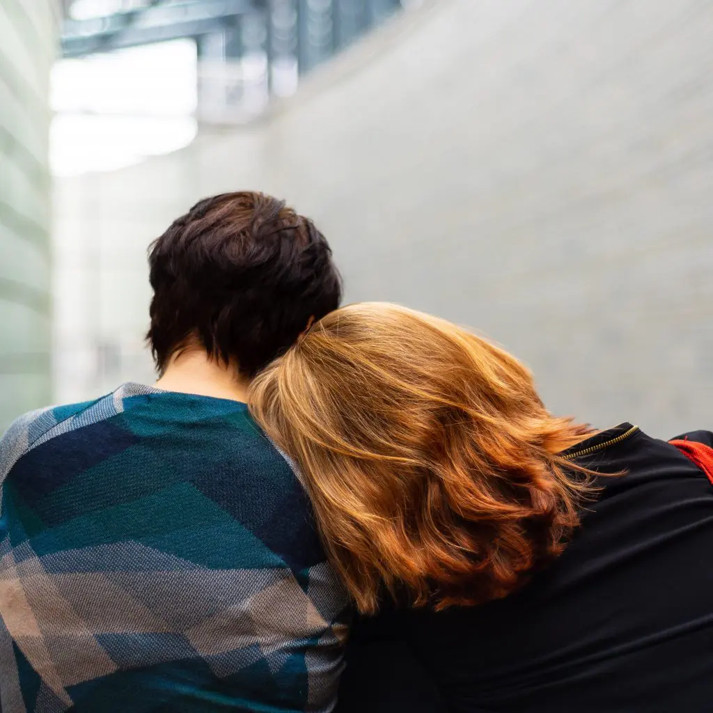 Grief affects everyone at one point. A person with red hair can be seen from behind leaning against a person with short brown hair.