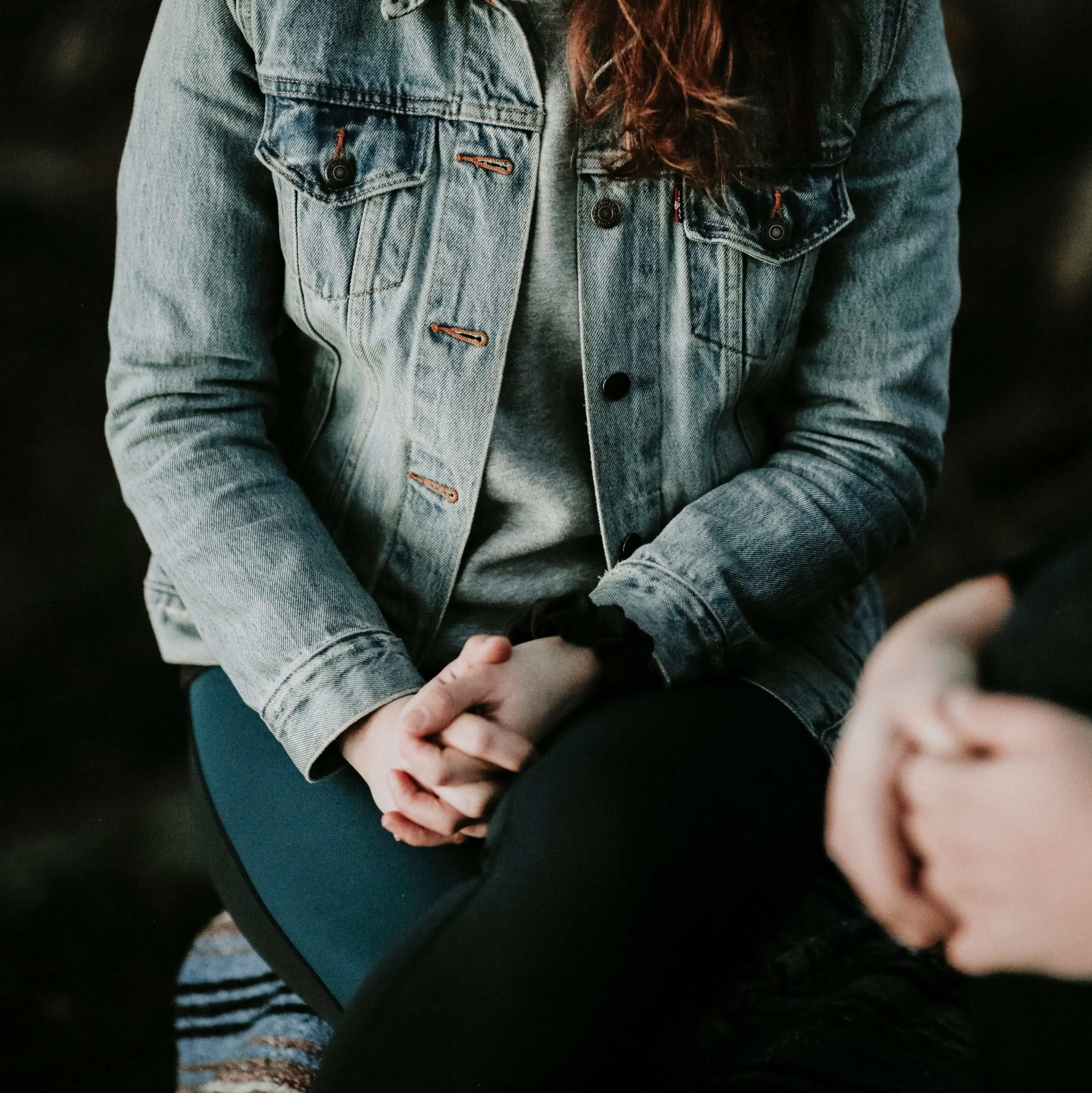 Two people sit with their hands clasped on their laps during therapy.